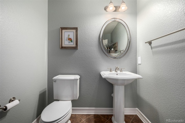 half bath with a sink, tile patterned flooring, toilet, and baseboards