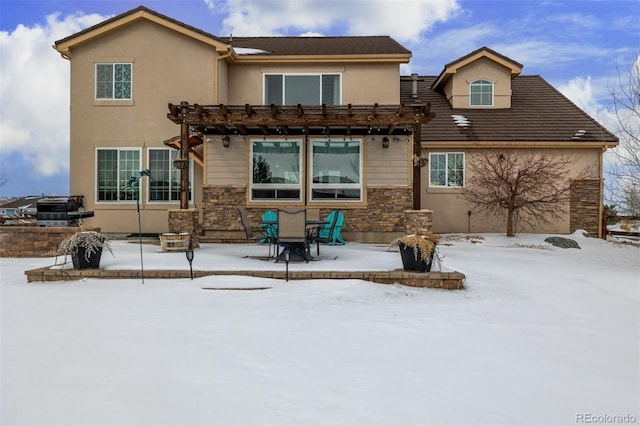 snow covered back of property featuring stone siding, stucco siding, and a pergola