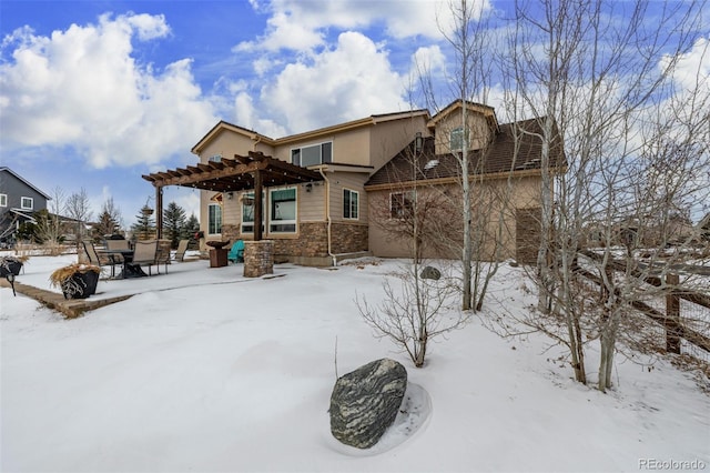 snow covered house with stone siding and a pergola