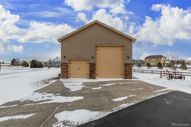 exterior space with a garage, stone siding, an outbuilding, fence, and stucco siding