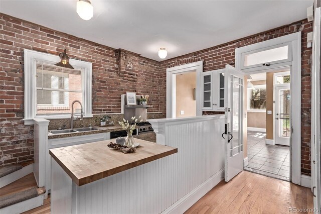 368 S Humboldt St, Denver, CO 80209 - kitchen with butcher block countertops, a sink, brick wall, light wood-style flooring, and glass insert cabinets