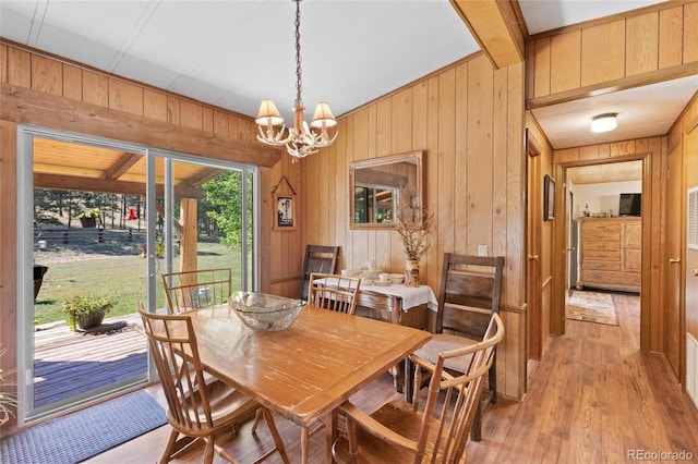 dining area with a notable chandelier, wood walls, and light hardwood / wood-style flooring