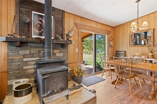 interior space with a wood stove, an inviting chandelier, decorative light fixtures, wooden walls, and light wood-type flooring