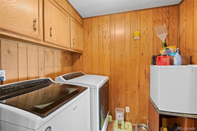 washroom featuring wooden walls, washer and clothes dryer, cabinets, and a textured ceiling