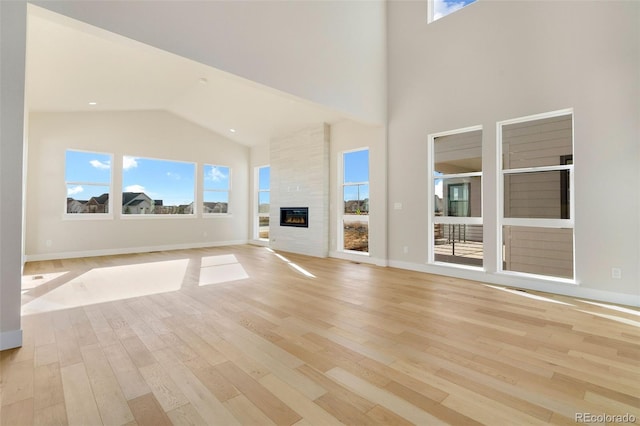 unfurnished living room with a fireplace, high vaulted ceiling, and light wood-type flooring