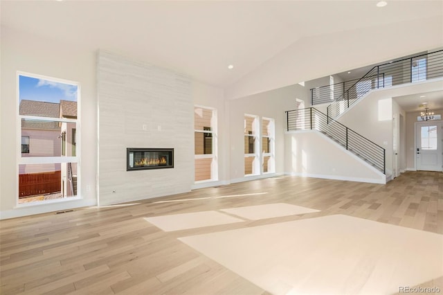 unfurnished living room featuring a tiled fireplace, plenty of natural light, high vaulted ceiling, and light hardwood / wood-style floors