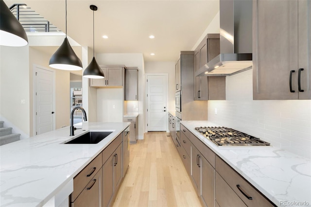 kitchen with sink, light hardwood / wood-style flooring, wall chimney exhaust hood, light stone countertops, and decorative light fixtures