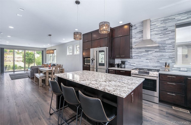2592 S Norse Ct, Lakewood, CO 80228 - kitchen with a center island, wall chimney range hood, a breakfast bar, stainless steel appliances, and decorative backsplash