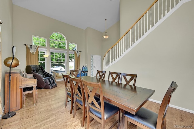 dining room with light wood-type flooring and a towering ceiling