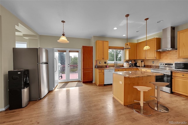 kitchen featuring wall chimney range hood, decorative light fixtures, light hardwood / wood-style flooring, and stainless steel appliances