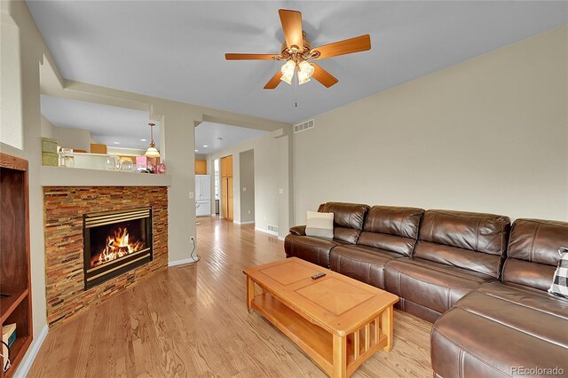 living room with a fireplace, ceiling fan, and light hardwood / wood-style floors