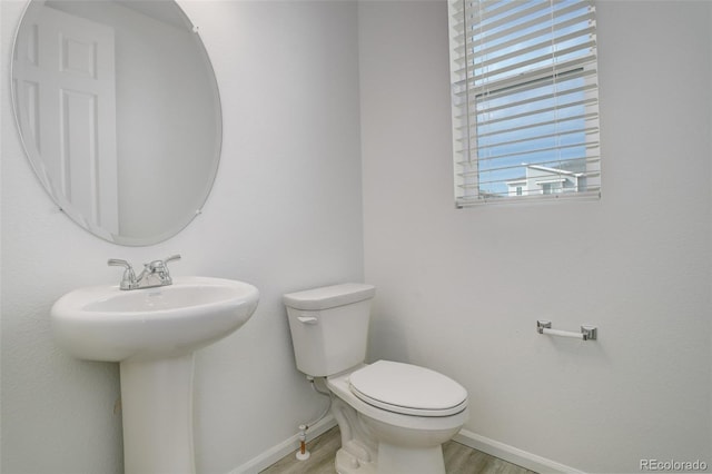 half bath with a sink, wood finished floors, toilet, and baseboards