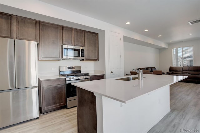 kitchen featuring stainless steel appliances, light countertops, open floor plan, a kitchen island with sink, and a sink