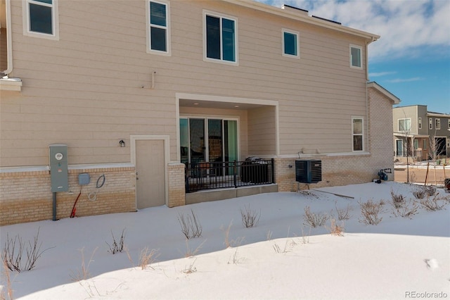 snow covered property with brick siding, fence, and central air condition unit