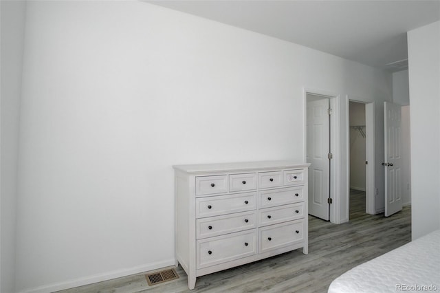 bedroom featuring light wood-style flooring, a spacious closet, visible vents, and baseboards