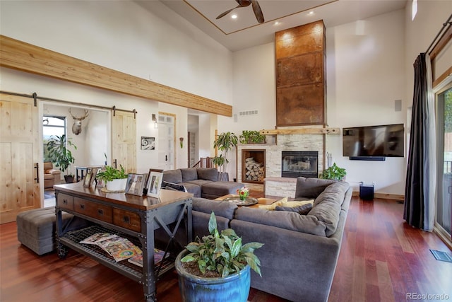 living room with a high ceiling, dark hardwood / wood-style flooring, a barn door, and a healthy amount of sunlight