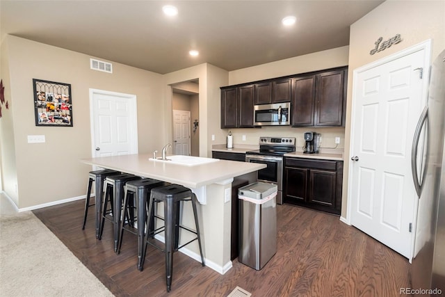 19468 E 65th Pl, Aurora, CO 80019 - kitchen with appliances with stainless steel finishes, a breakfast bar, dark brown cabinetry, dark wood-style floors, and recessed lighting