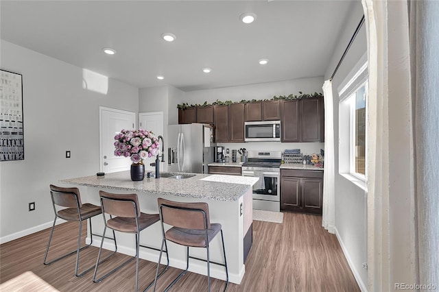 kitchen with a kitchen island with sink, dark brown cabinets, stainless steel appliances, a kitchen breakfast bar, and light hardwood / wood-style floors