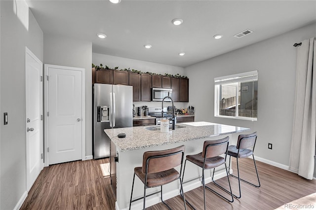 kitchen featuring appliances with stainless steel finishes, a breakfast bar area, a center island with sink, and dark brown cabinetry