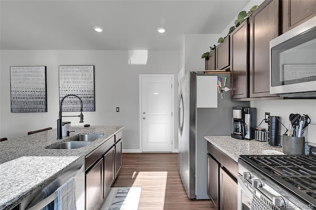 kitchen with appliances with stainless steel finishes, sink, dark brown cabinetry, light stone countertops, and dark wood-type flooring