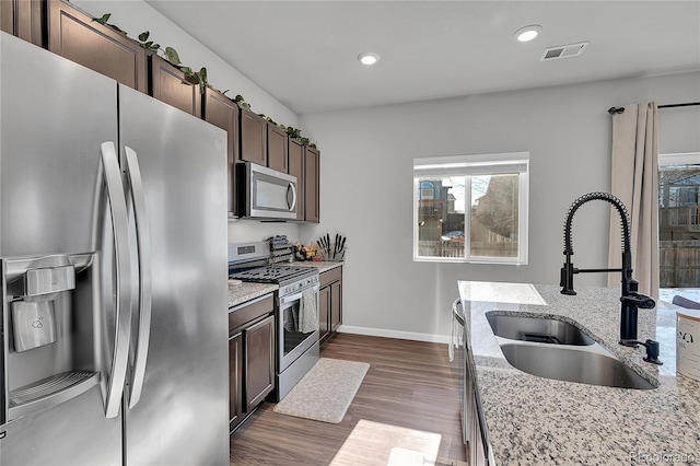 kitchen featuring sink, light stone counters, dark brown cabinets, appliances with stainless steel finishes, and dark hardwood / wood-style floors