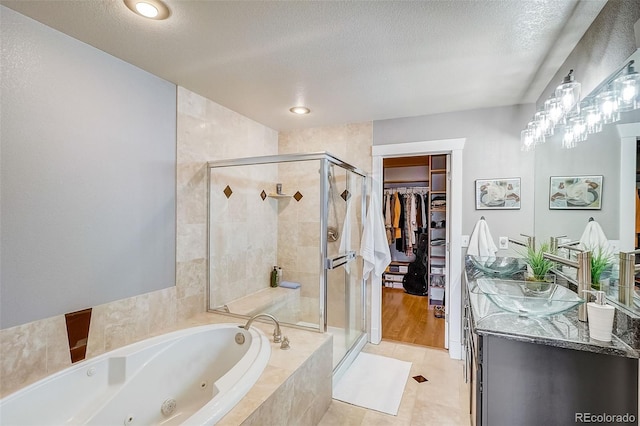 full bath with a walk in closet, a stall shower, a textured ceiling, vanity, and a jetted tub