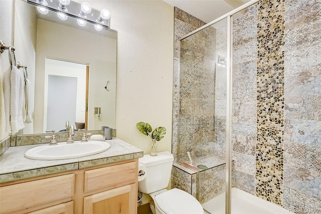 full bathroom featuring toilet, a stall shower, a textured wall, and vanity