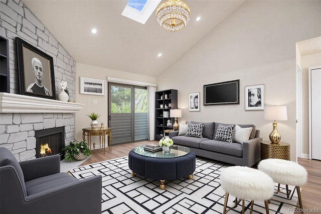 living area with high vaulted ceiling, wood finished floors, a skylight, a stone fireplace, and a chandelier