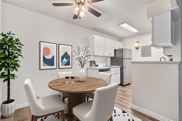 dining room featuring a ceiling fan, light wood finished floors, a textured ceiling, and baseboards