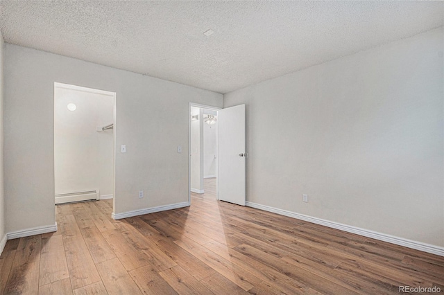 spare room with a baseboard radiator, hardwood / wood-style floors, baseboards, and a textured ceiling
