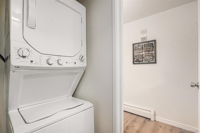 laundry room with stacked washer / dryer, baseboard heating, light wood-type flooring, and baseboards