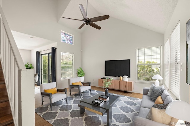 living area with wood finished floors, high vaulted ceiling, stairs, and a ceiling fan
