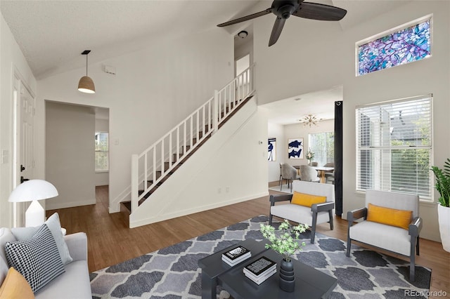 living area with stairs, wood finished floors, high vaulted ceiling, ceiling fan, and baseboards