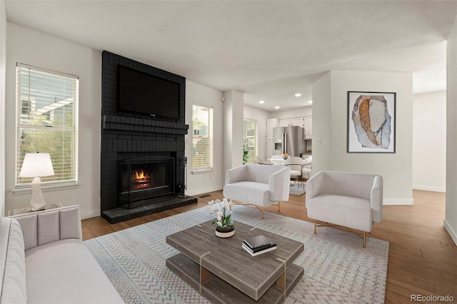 living room featuring baseboards, a brick fireplace, light wood-style floors, and recessed lighting