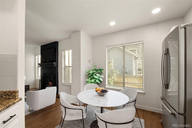 dining space with dark wood-type flooring, a large fireplace, baseboards, and recessed lighting