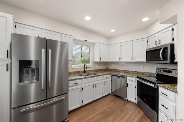 kitchen featuring stainless steel appliances, a sink, white cabinetry, dark wood finished floors, and dark stone countertops