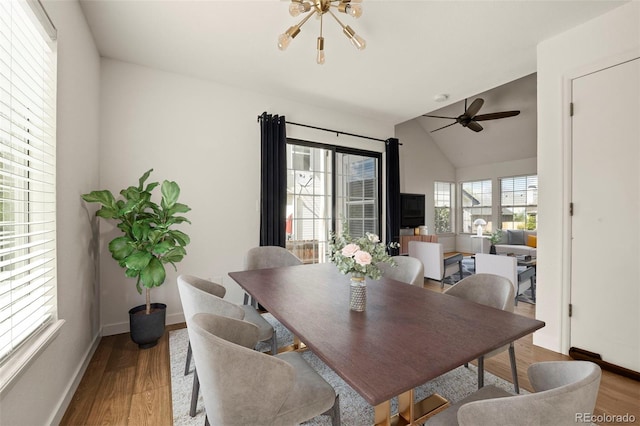 dining room with wood finished floors, baseboards, a ceiling fan, vaulted ceiling, and a chandelier