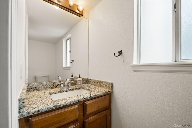 half bath featuring vanity, toilet, and a textured wall