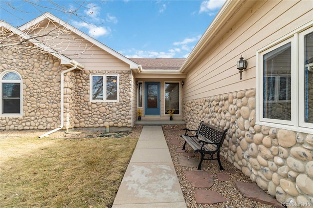 entrance to property featuring stone siding, a lawn, and a shingled roof