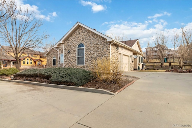 view of side of home featuring stone siding, concrete driveway, a garage, and fence