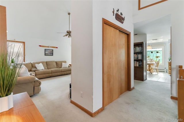 hall featuring a baseboard heating unit, light carpet, a high ceiling, and baseboards