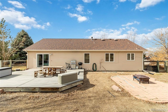 back of property with a shingled roof, a wooden deck, fence, and an outdoor fire pit