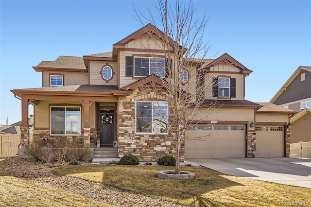 craftsman house with stone siding, covered porch, fence, and concrete driveway