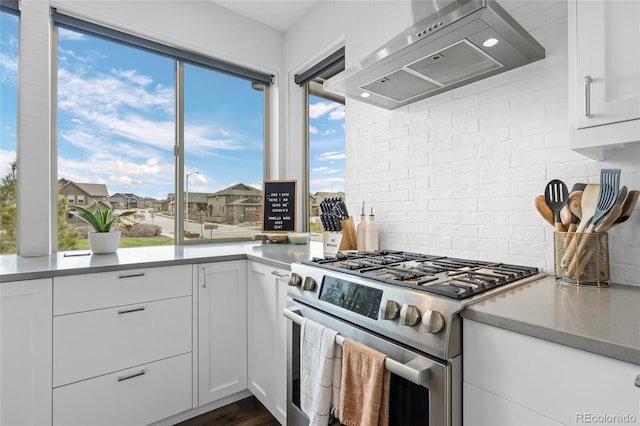 kitchen with stainless steel range with gas cooktop, white cabinets, a healthy amount of sunlight, and wall chimney exhaust hood