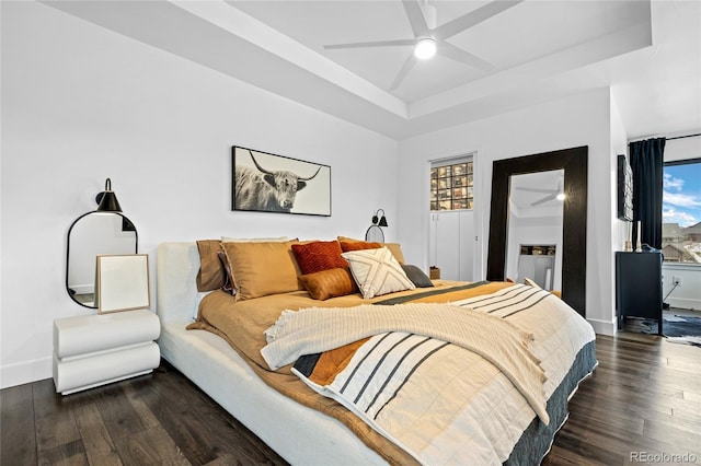bedroom featuring a raised ceiling, ceiling fan, wood finished floors, and multiple windows