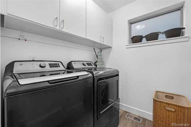 clothes washing area with cabinet space, baseboards, wood finished floors, visible vents, and washer and clothes dryer