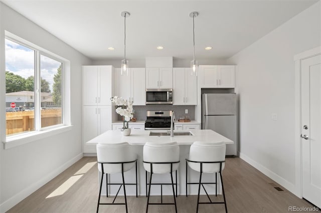 kitchen featuring white cabinetry, an island with sink, appliances with stainless steel finishes, and decorative light fixtures