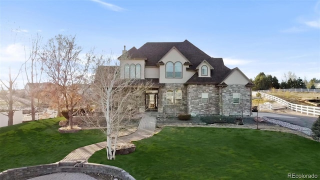 french provincial home with stone siding, fence, a front lawn, and stucco siding