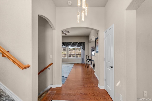 hallway featuring arched walkways, wood finished floors, and baseboards