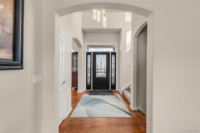 entryway featuring baseboards, arched walkways, and wood finished floors